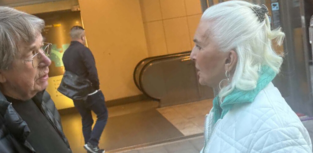 Kungaväninnan stannar för en pratstund på Östermalm. Det silvervita håret är uppsatt med en dekorativ klämma, med mjukt böjda längder i nacken.